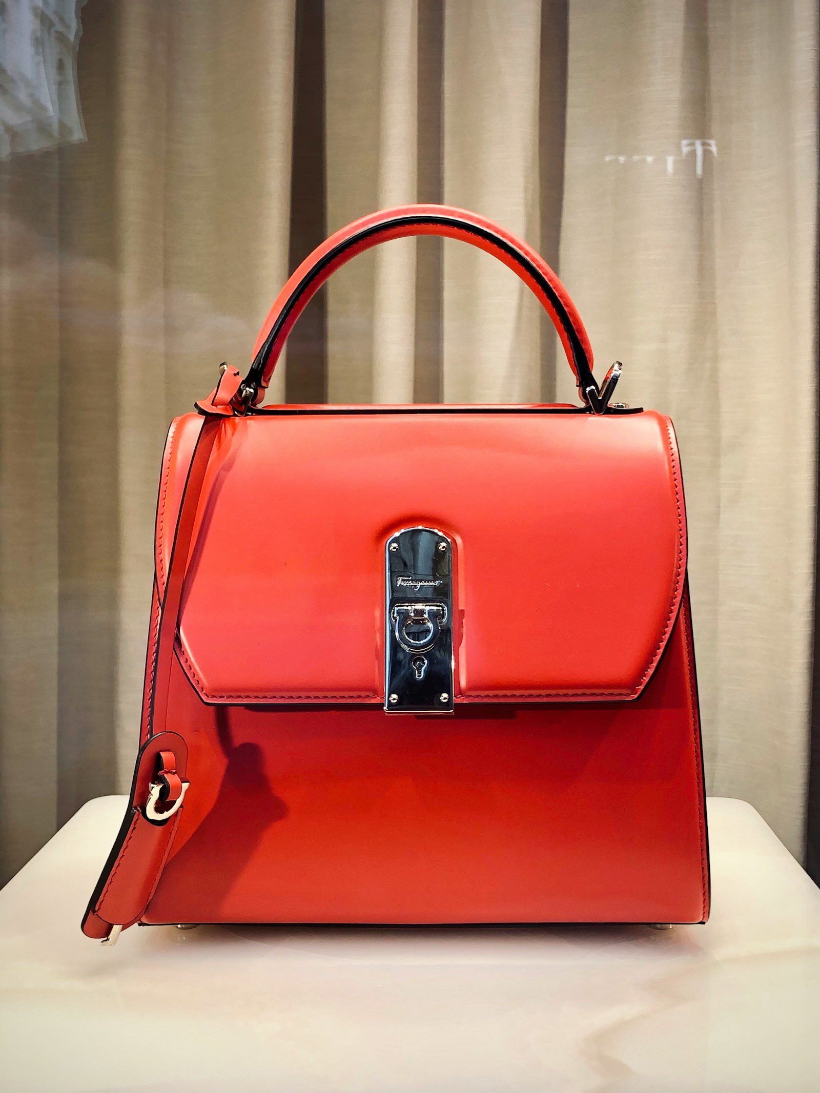 Red leather designer handbag on a white table showing handbag size and structure