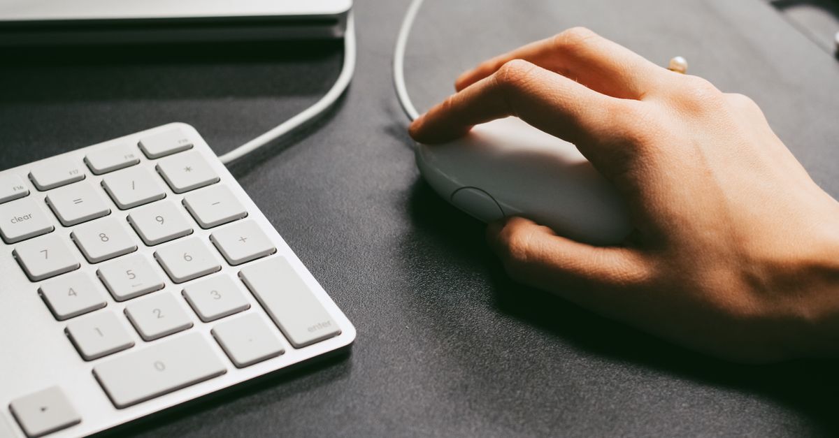 Close-up of a hand operating a standard computer mouse beside a keyboard