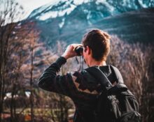 Man using binoculars for wildlife viewing near forest trees