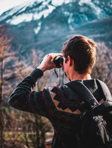 Man using binoculars for wildlife viewing near forest trees